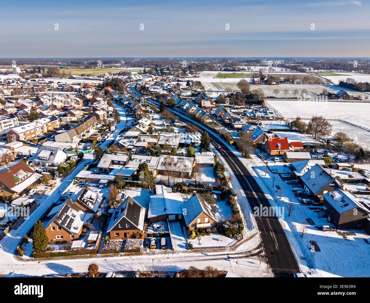 Vista aerea di una tranquilla cittadina europea dopo una nevicata. L'immagine mostra i tetti innevati, le strade asfaltate pulite e i campi soleggiati che si estendono fino al Foto Stock