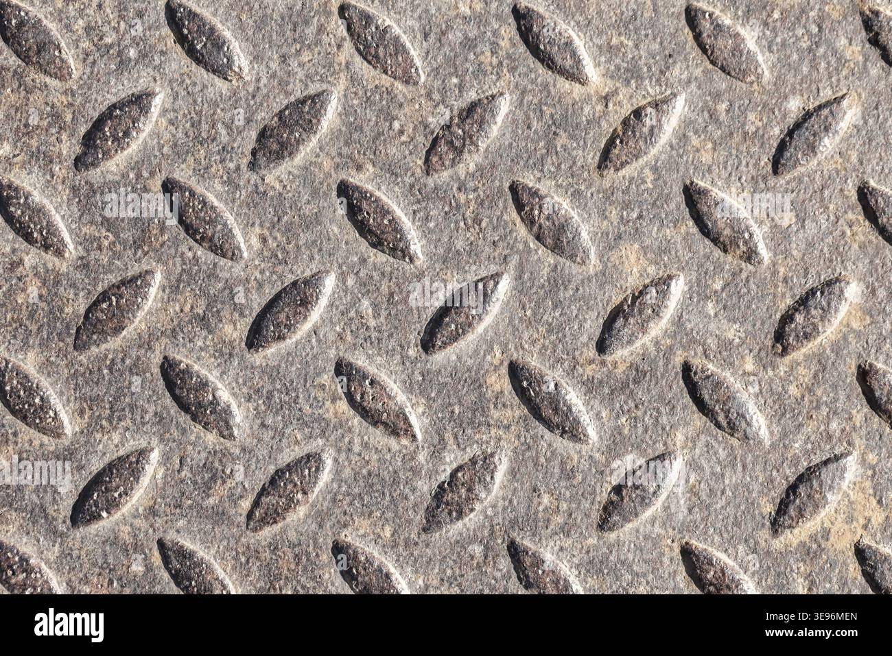 Primo piano di una piastra diamantata in metallo che mostra uno schema del battistrada ovale rialzato su una superficie in acciaio resistente agli agenti atmosferici. Texture grintosa e industriale ideale per sfondi, de Foto Stock