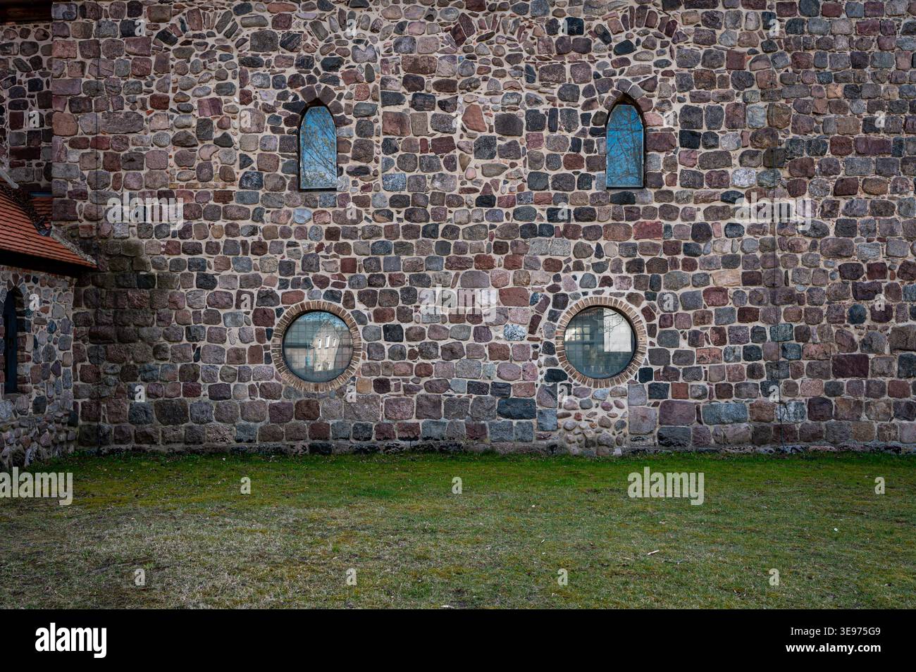 Dettaglio della facciata della storica chiesa in pietra di campo a Lindenberg, Germania, con tre finestre ad arco sopra due finestre circolari. Foto Stock