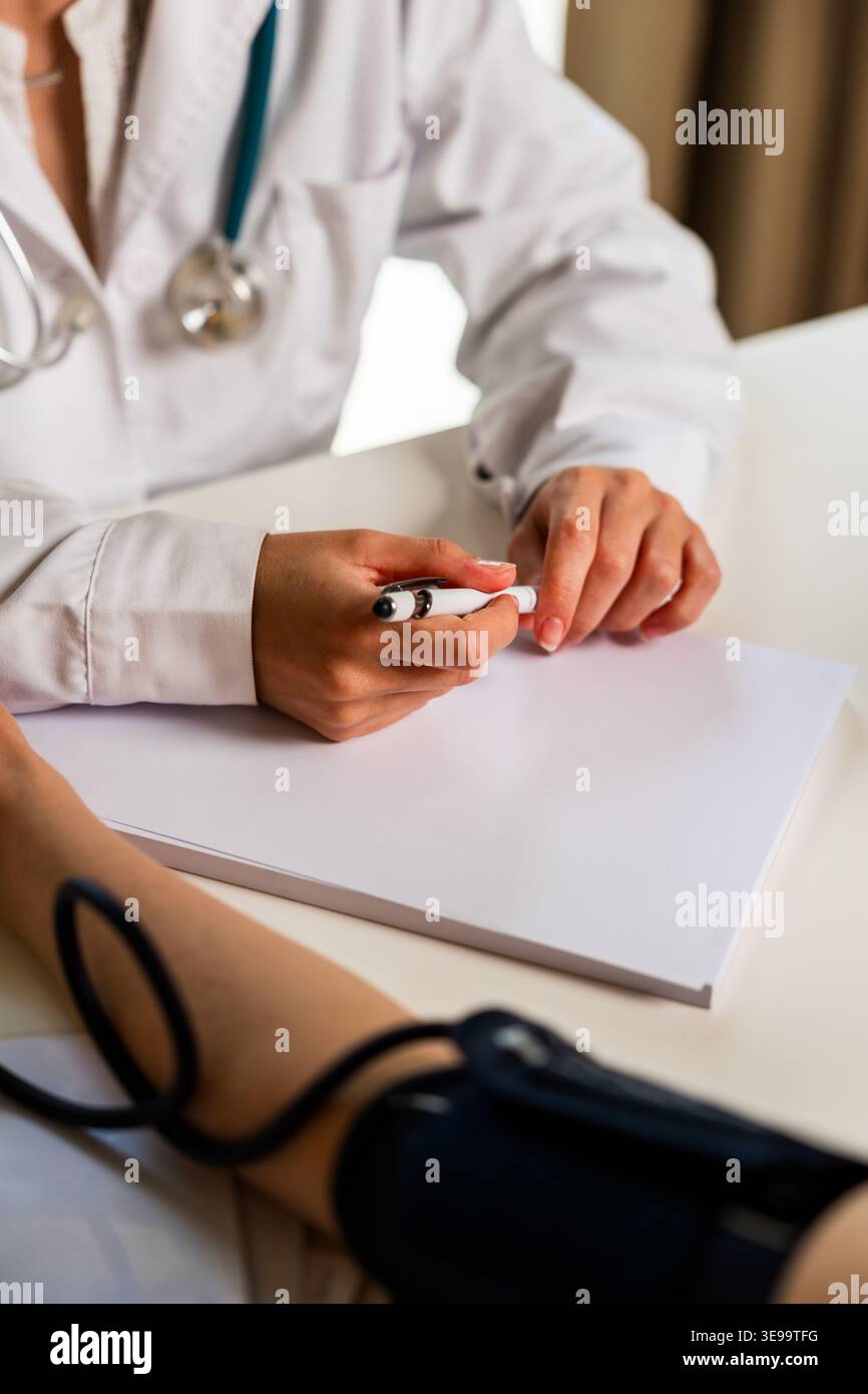 Medico che controlla la pressione sanguigna e scrive note mediche Foto Stock