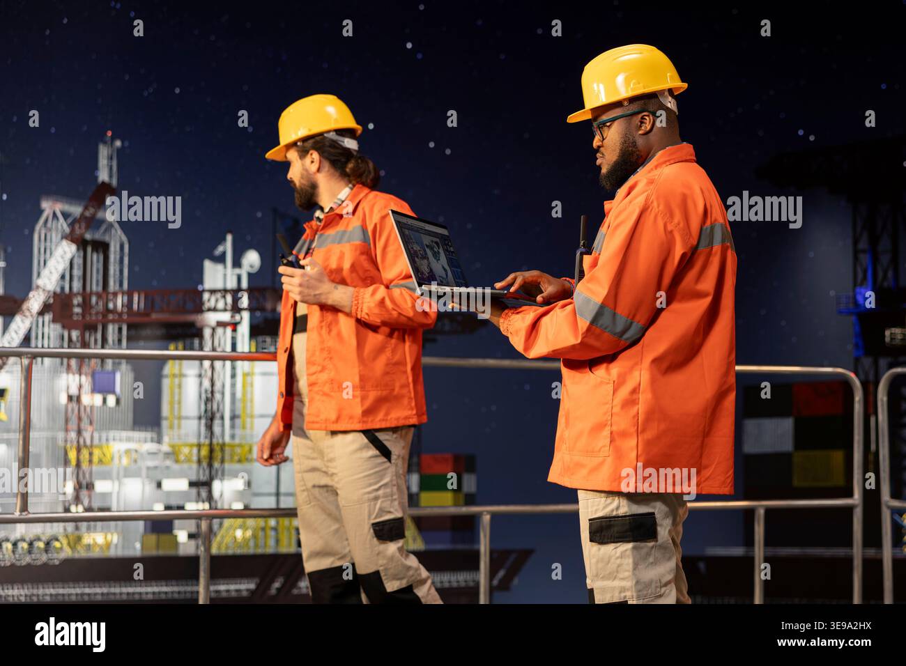 Il team di ingegneria delle chiatte sulla piattaforma offshore che utilizza un computer portatile per supervisionare le operazioni di perforazione durante il turno di notte. I colleghi addetti alla perforazione delle chiatte che esaminano i dati dei sensori su un notebook per garantire una produzione continua Foto Stock