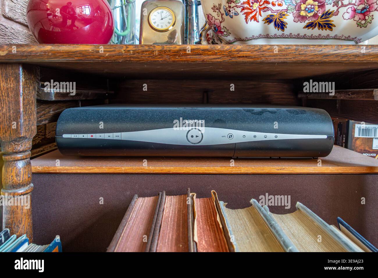 Un decoder Sky+HD vecchio, polveroso e obsoleto si trova su uno scaffale accanto a ornamenti e vecchi libri. Foto Stock