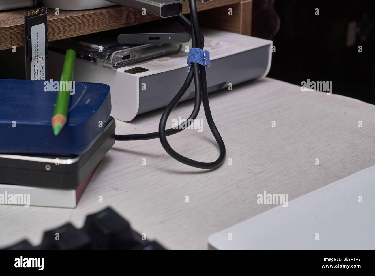 Una scrivania bianca visualizza vari dispositivi di storage, dagli HDD impilati a un moderno SSD NVMe. Cavi e una matita verde completano questo autentico spazio di lavoro IT. Foto Stock