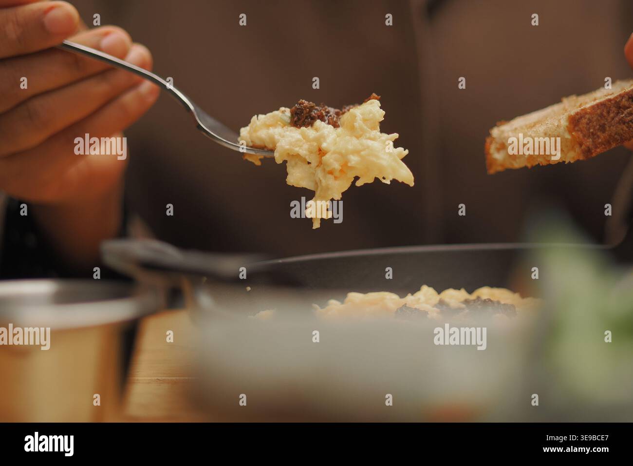 donna che tiene in mano una forchetta con uova strapazzate e un pezzo di pane durante la colazione Foto Stock