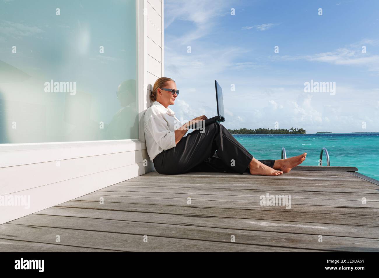 Donna sorridente e di successo con un notebook su una splendida spiaggia soleggiata. Successo. Lavoro a distanza flessibile, concetto di equilibrio tra lavoro e vita privata femminile. Foto Stock