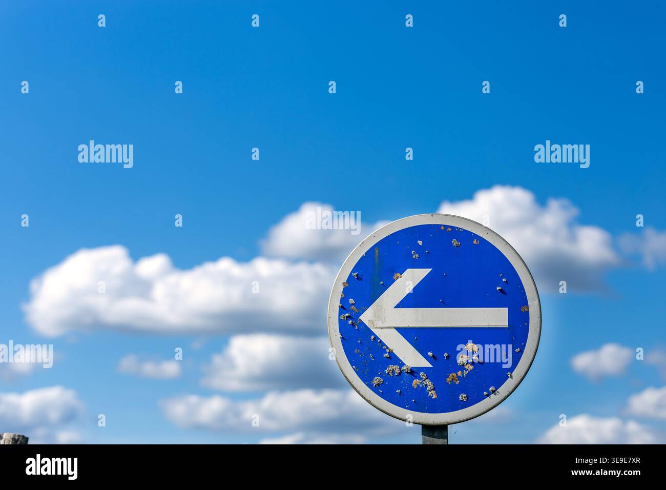 Un cartello stradale blu si erge su uno sfondo morbido di un cielo blu brillante con soffici nuvole bianche. La composizione minimalista enfatizza Foto Stock