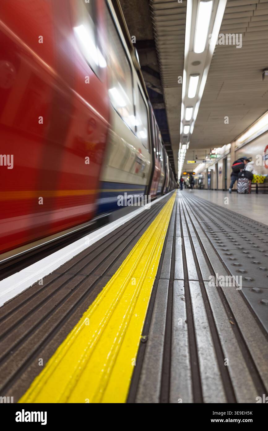 Treno rosso sfocato che supera una linea di sicurezza gialla su una piattaforma Foto Stock