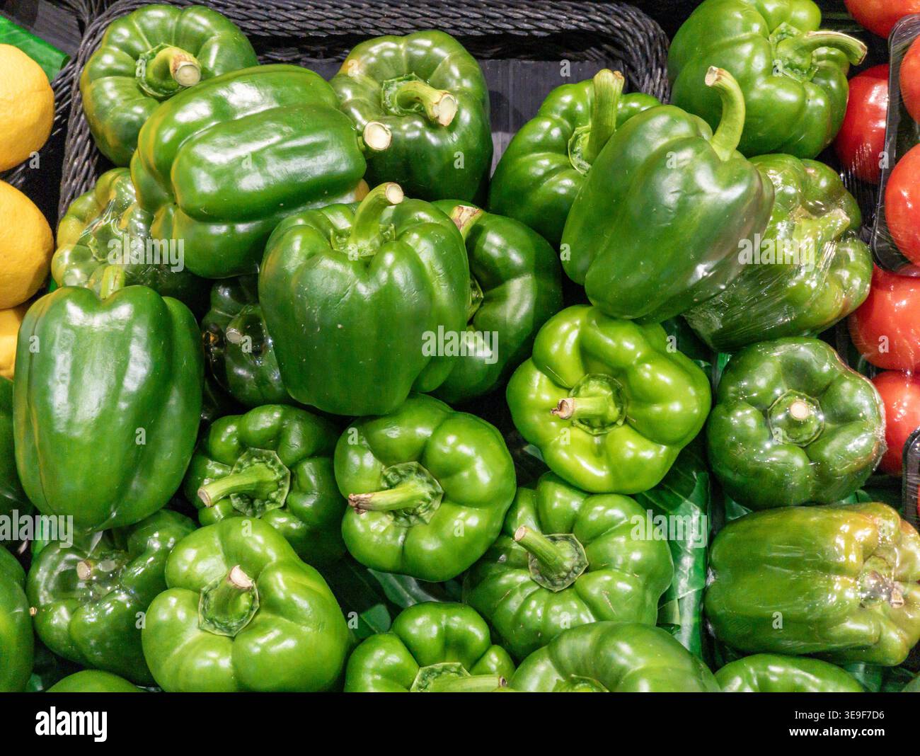Vista ravvicinata di peperoni verdi freschi e lucidi accatastati in un cestino in tessuto scuro presso un supermercato o un negozio di alimentari. Foto Stock