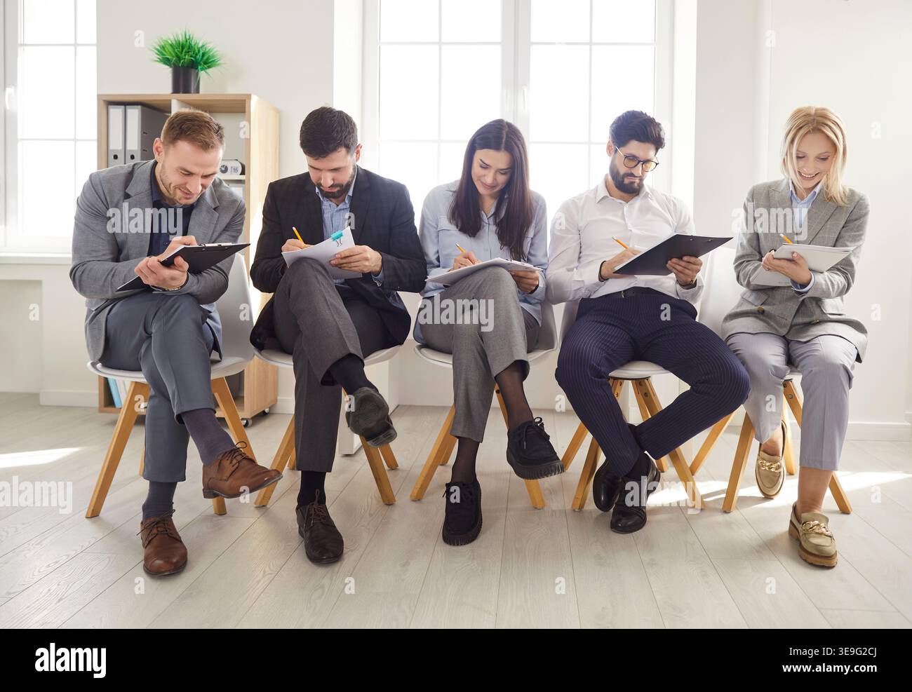 Persone diverse su sedie in fila in attesa di un colloquio di lavoro entrano in ufficio, i candidati Foto Stock