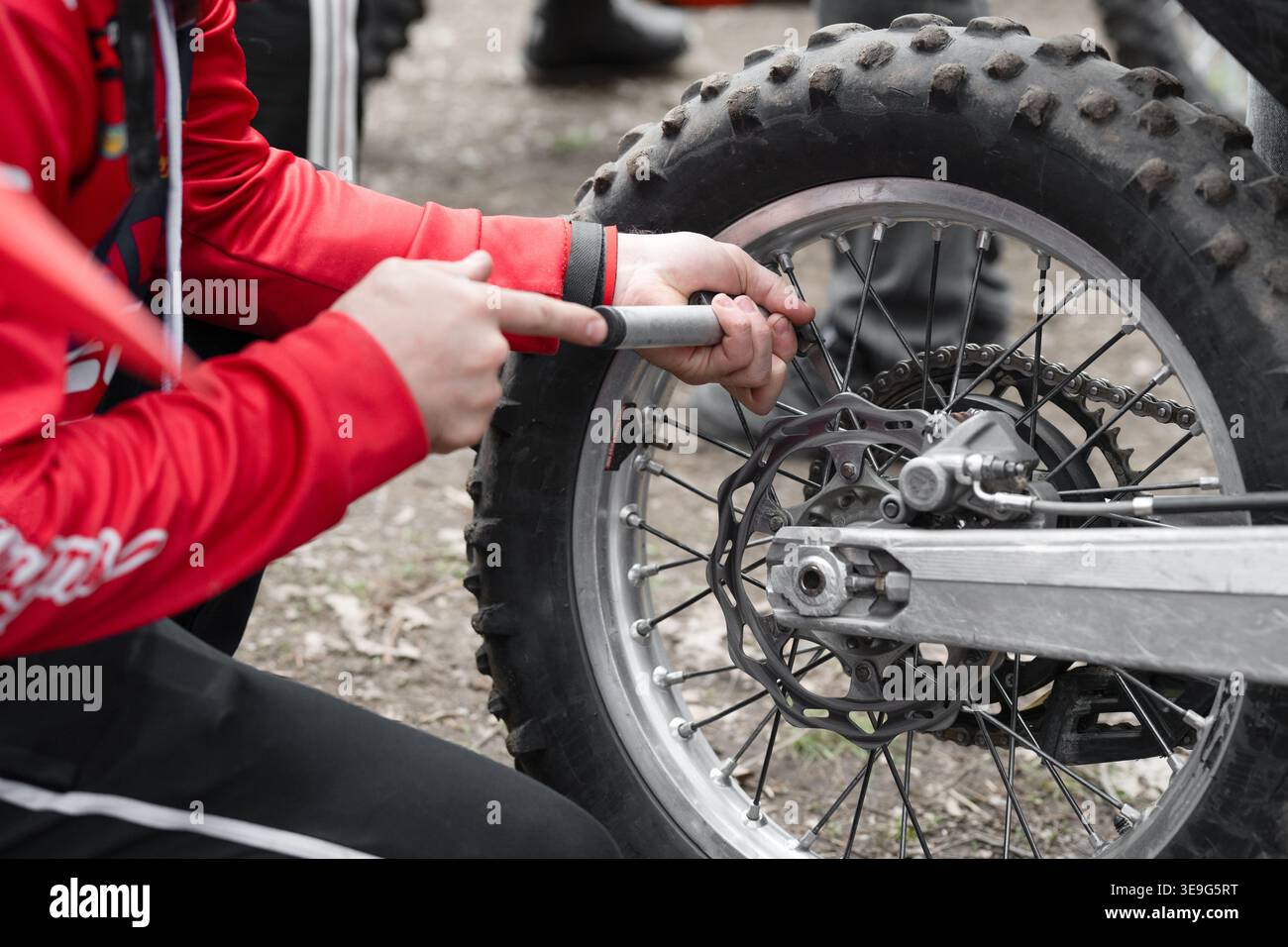 Mani del meccanico che regolano i raggi sulla ruota posteriore di una moto da motocross. Primo piano di una persona in maglia rossa che esegue la manutenzione tecnica su una moto da terra r Foto Stock