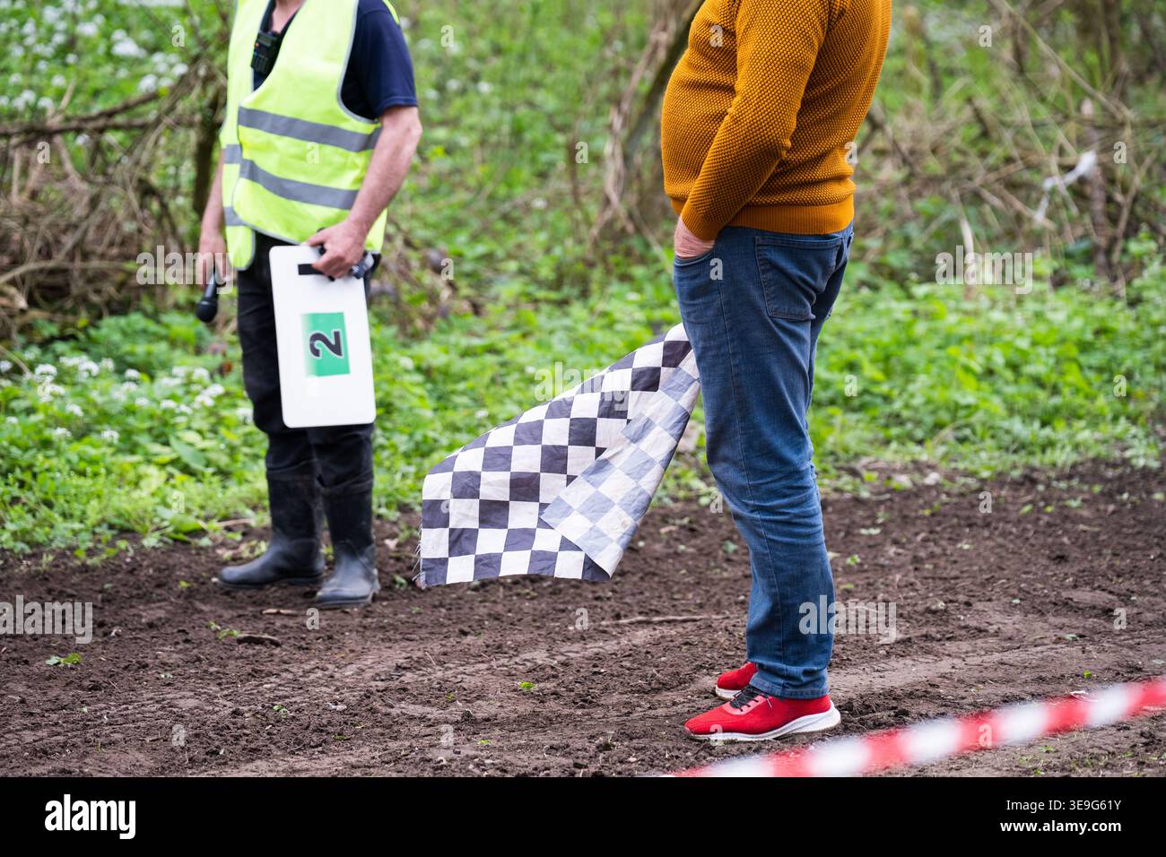 Ufficiale sportivo con bandiera a scacchi in piedi su una pista sterrata. Momento di tensione prima della gara con sceriffi, bandiera a scacchi e equipaggiamento di segnalazione Foto Stock