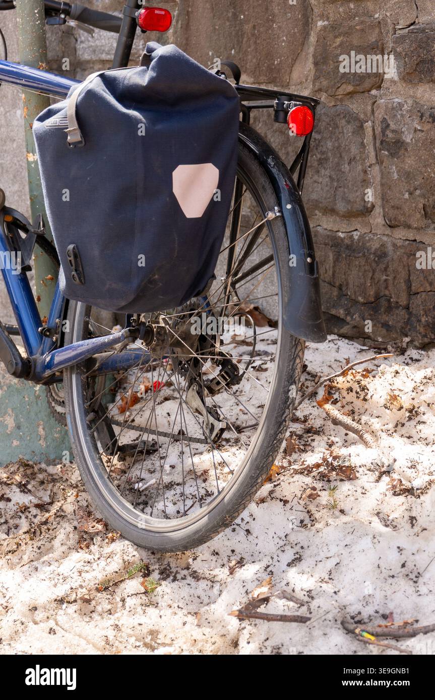 Bicicletta Blue Commuter con Pannier Bag parcheggiata in Dirty Urban Snow contro Stone Wall Foto Stock