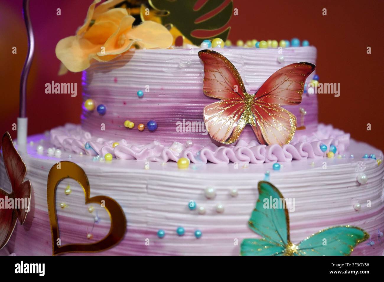 Primo piano della torta di festa a livelli viola con farfalla decorativa e copricuore Foto Stock