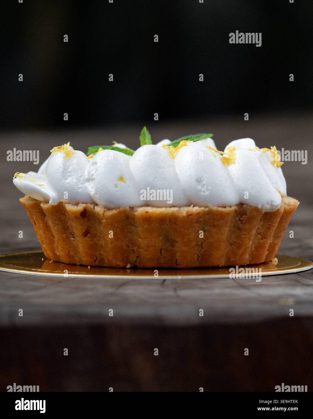 Crostata delicata con meringa cremosa ed erbe fresche. La crosta dorata si trova su una superficie rustica in legno. L'illuminazione soffusa mette in risalto l'invitante consistenza del dessert. P Foto Stock