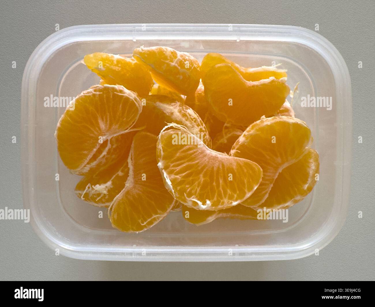 Segmenti di arancio mandarino sbucciati in un contenitore di plastica trasparente, vista dall'alto verso il basso, snack salutari o concetto di cestino per pranzo. Foto Stock