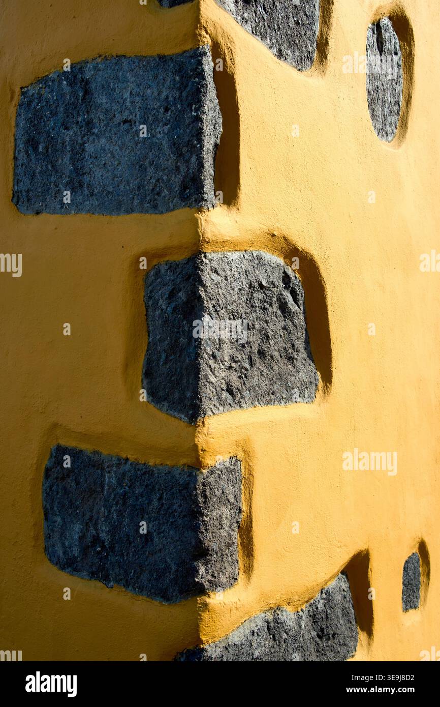 Primo piano di una parete angolare con pietre grigie incastonate in gesso giallo. Dettagli architettonici mediterranei tradizionali con texture ruvida. Foto Stock