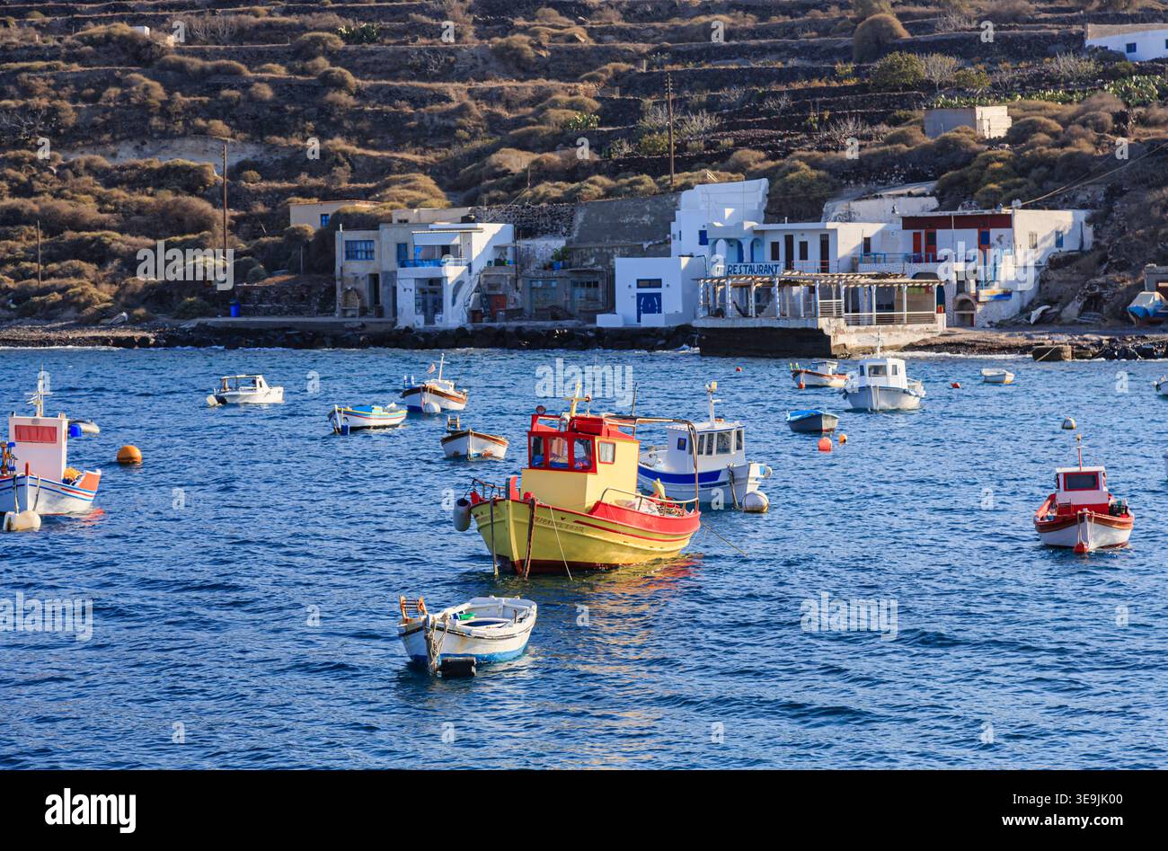 Piccolo ristorante locale imbiancato sulla costa e barche da pesca ormeggiate dal villaggio di Korfos, Thirassia, Santorini nelle Cicladi greche Foto Stock