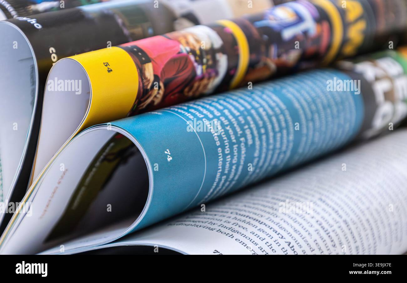 riviste lucide arrotolate impilate con pagine vivaci e profondità di campo ridotta. Concetto di supporti di stampa, pubblicazione, lettura e progettazione. Foto Stock