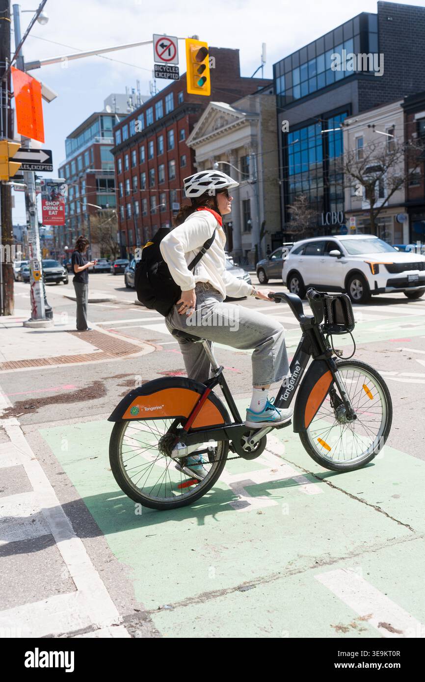 Toronto, Canada - 17 aprile 2026: Pendolari del giorno corrente su una vivace bicicletta arancione che si muove attraverso l'energica Toronto Foto Stock