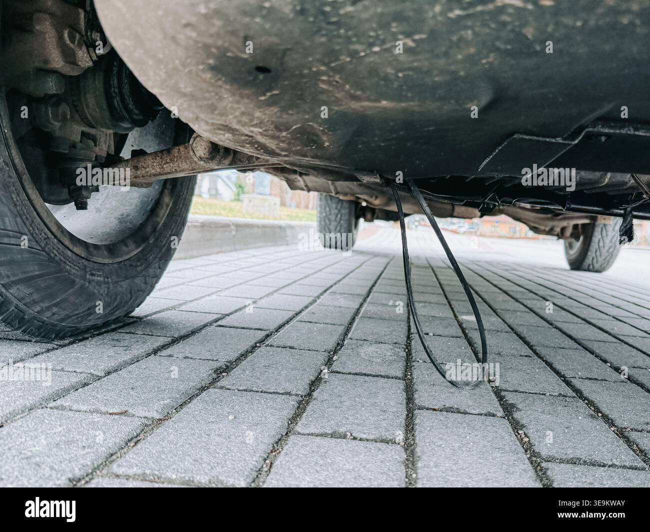 Vista ad angolo basso del carro di un'auto con un cavo sospeso allentato vicino alla ruota su una superficie pavimentata. Evidenzia i problemi di manutenzione del veicolo, meccanici Foto Stock