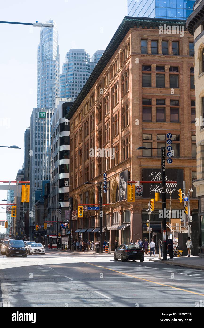 Toronto, Canada - 17 aprile 2026: Incrocio illuminato dal sole con calde attrazioni architettoniche e pendolari al telefono Foto Stock