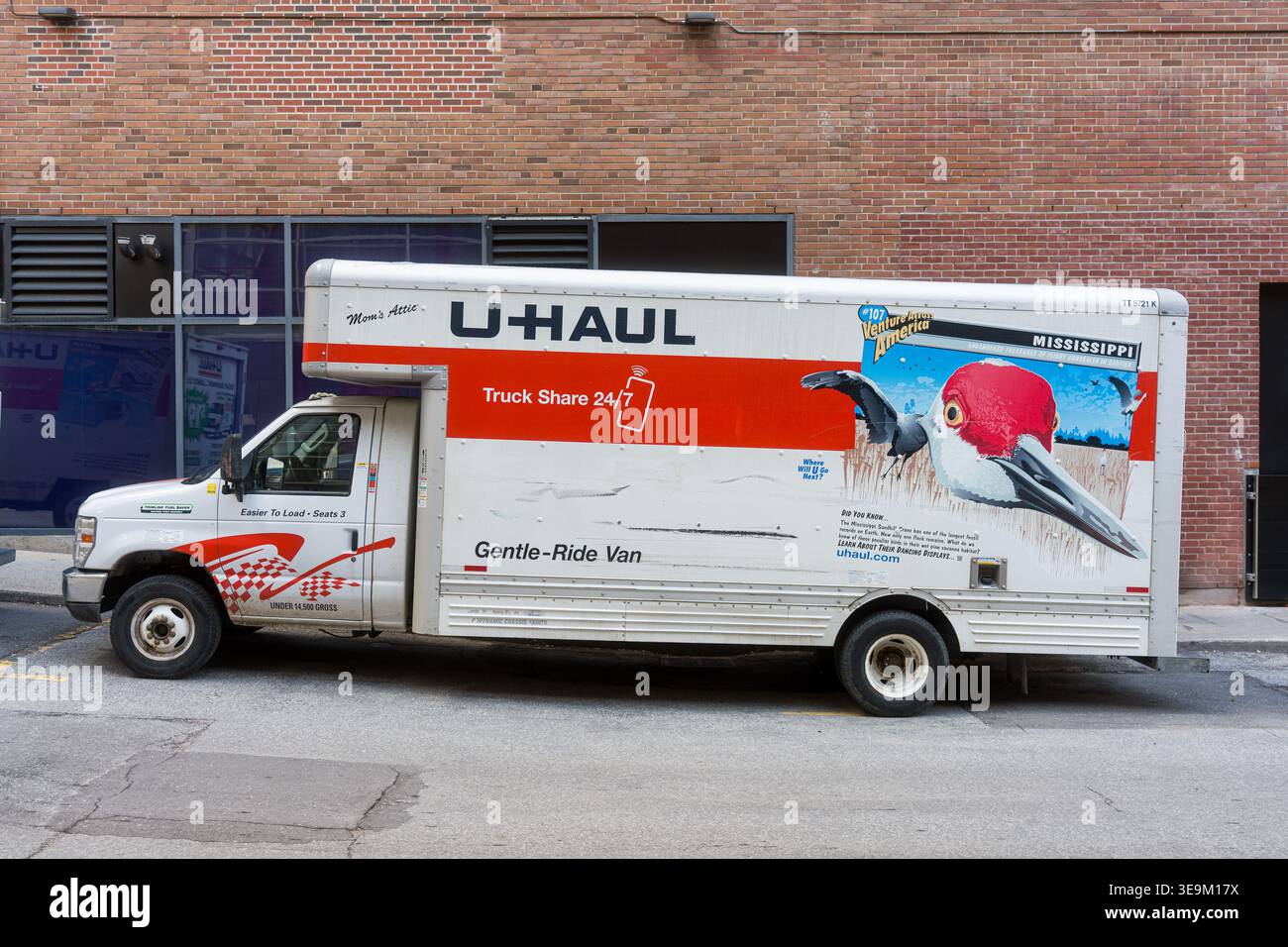 Toronto, Canada - 17 aprile 2026: Veicolo VIVID UHaul con illustrazione di uccelli tropicali contro il magazzino di mattoni della città Foto Stock