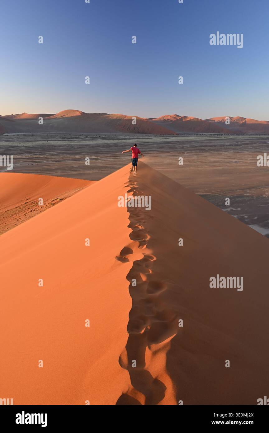 Uomo che cammina lungo la cresta delle dune al tramonto, Sossusvlei, Namib-Naukluft National Park, Namibia Foto Stock