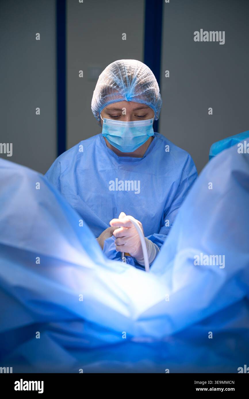 Donna caucasica in abbigliamento chirurgico che tiene lo strumento in sala operatoria Foto Stock