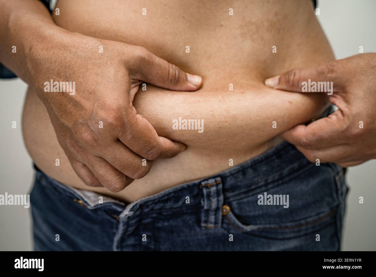 Donna asiatica sovrappeso mostra e usa la mano per spremere il ventre grasso. Foto Stock