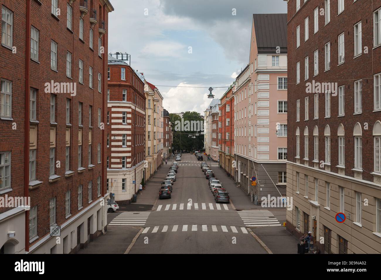 HELSINKI, FINLANDIA - 11 AGOSTO 2025: Lunga strada residenziale alberata con condomini rossi e bianchi che svaniscono in un punto di scomparsa. Foto Stock