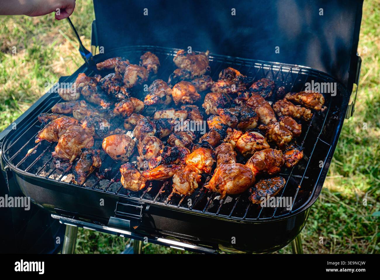 Gambe di pollo piccanti e ali grigliate su un fuoco fumante in un barbecue portatile. Foto Stock