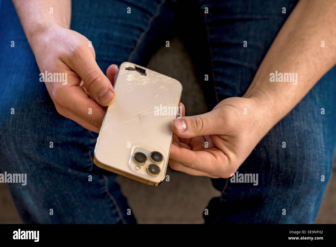 Riparazione necessaria per il telefono rotto. La persona interessata esamina attentamente lo smartphone danneggiato con bordi rigati. Scena casual in interni che mostra frustrazione Foto Stock