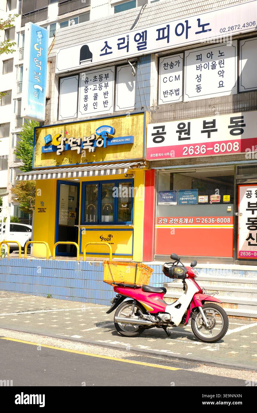 Facciata gialla vibrante di uno snack bar locale (negozio Tteokbokki) a Seoul, con uno scooter rosso parcheggiato di fronte, che illustra il cibo della città Foto Stock