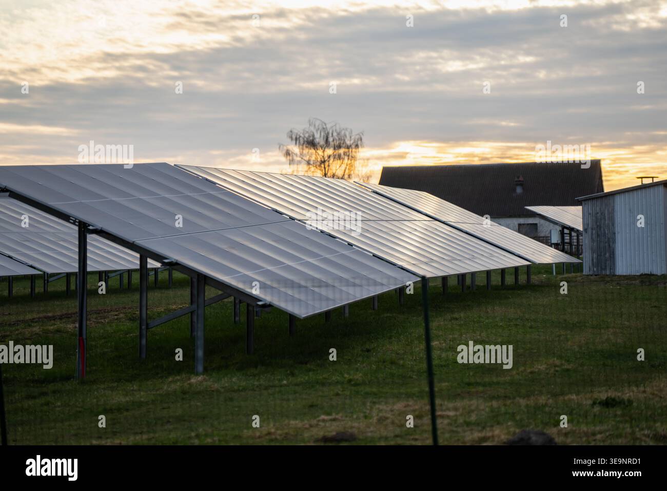 Installazione di impianti solari con moduli fotovoltaici angolati su supporti metallici in prossimità di case rurali e capannoni per temi di mercato della produzione di energia elettrica sostenibile oggi Foto Stock