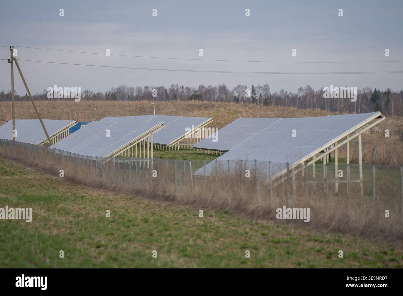 Grandi array di pannelli fotovoltaici installati su terreni di campagna con supporti metallici, erba secca, linee elettriche e vista produzione di elettricità pulita Foto Stock
