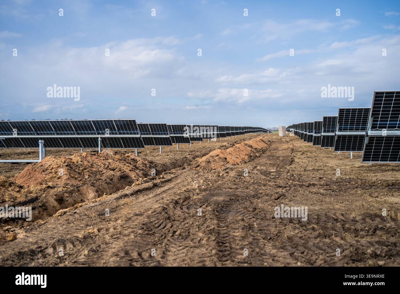 Strada per la costruzione di impianti solari tra lunghe file di pannelli fotovoltaici con cingoli fangosi, pali di terreno e siti di energia rinnovabile su scala utility Foto Stock