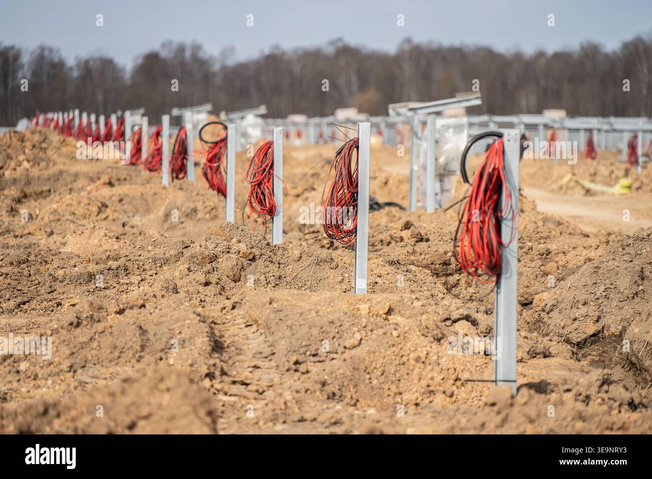 Sito fotovoltaico con bobine rosse ripetute su pali di fondazione in acciaio, file di terreno accidentato e vista dell'hardware di montaggio dell'inseguitore solare Foto Stock