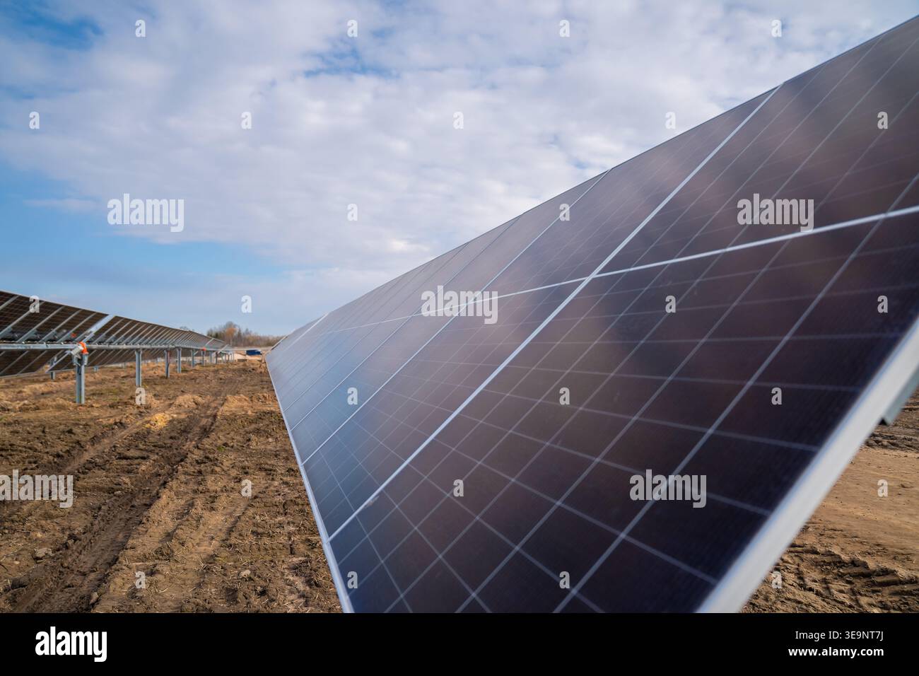 Lunga fila di moduli solari inclinati con vetro a griglia accanto a un terreno di costruzione ruvido per lo sviluppo di centrali elettriche pulite e temi infrastrutturali Foto Stock
