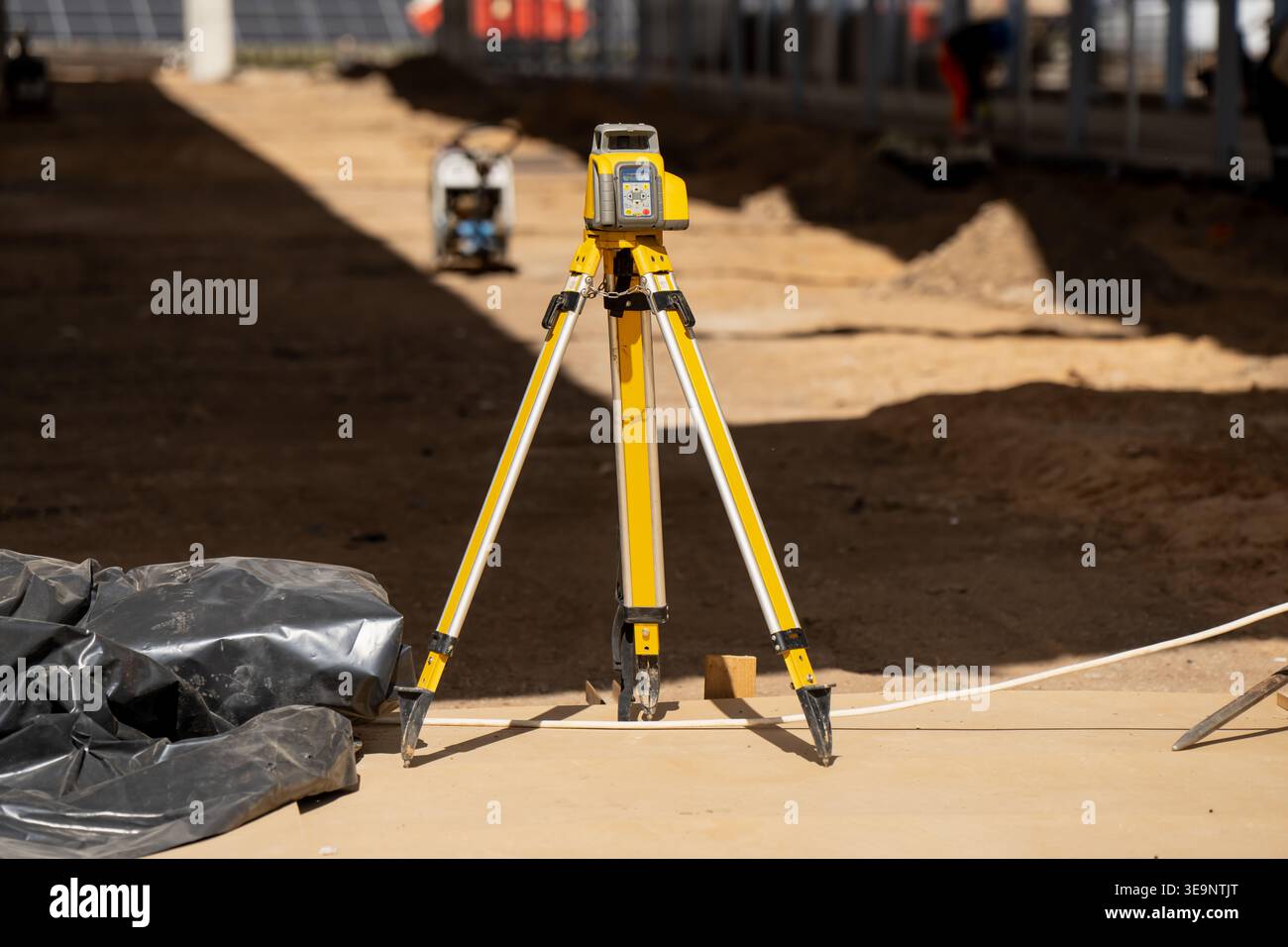 Livella laser per rilievi edili su treppiede giallo in piedi su piattaforma di lavoro in compensato per livellamento, allineamento e scale solari Foto Stock