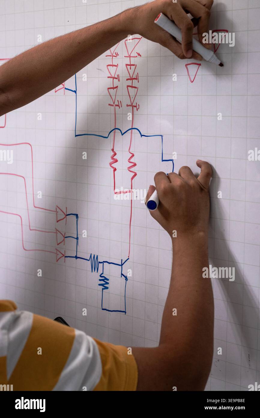 Una persona sta disegnando uno schema elettrico su una lavagna bianca. Il disegno è colorato e include una linea rossa e blu. La persona sta usando un marcatore per disegnare Foto Stock