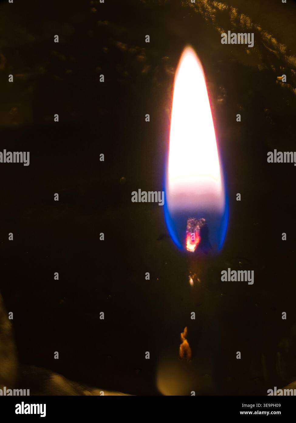Primo piano di una brillante fiamma di candele con toni blu e arancioni accesi su uno sfondo di cera scuro e ruvido. Simbolico di speranza, fede, e m Foto Stock