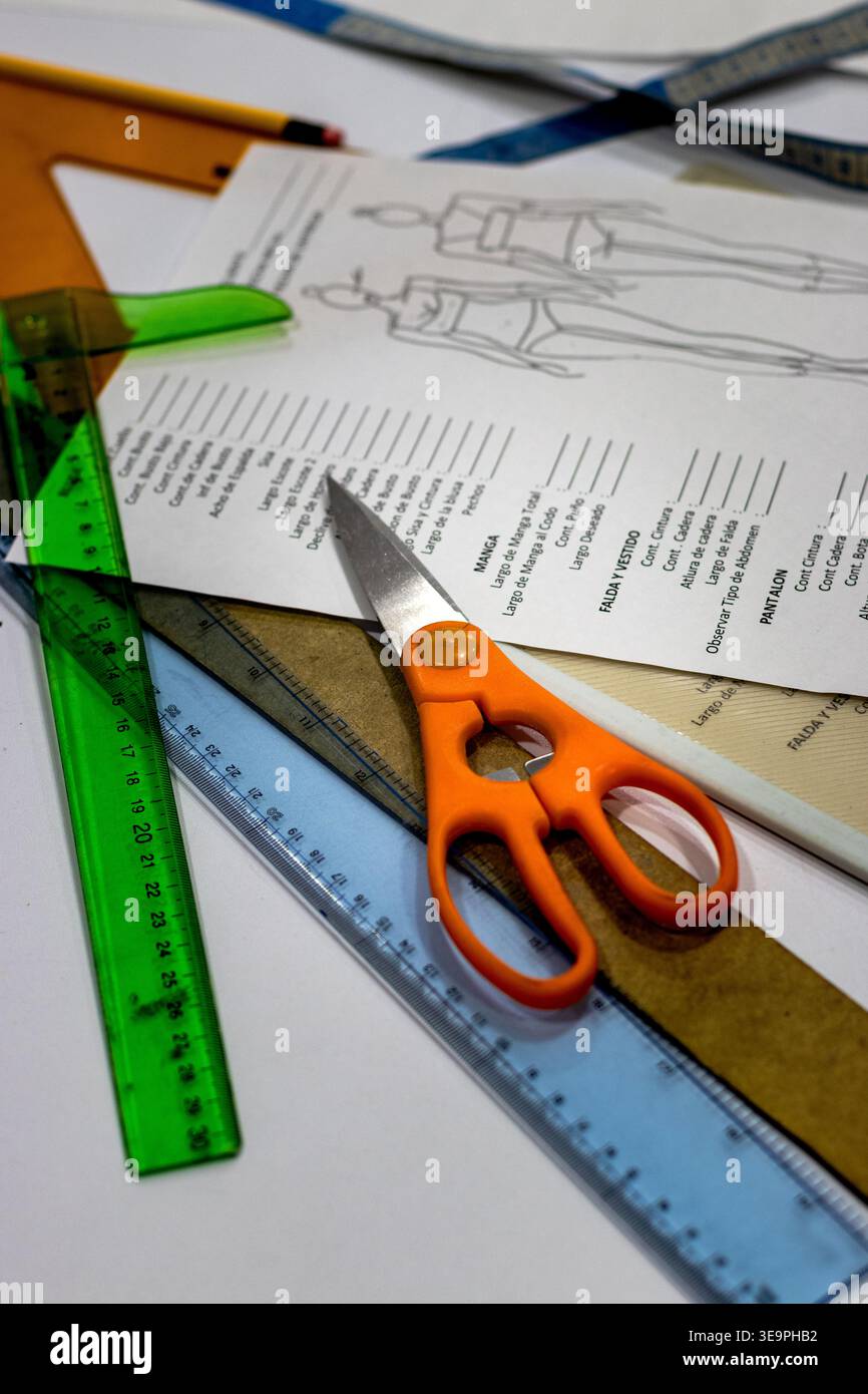 Un'area di lavoro con gli strumenti essenziali per la personalizzazione, tra cui forbici, righelli e un foglio di fantasia con le misure degli indumenti. Ideale per t Foto Stock