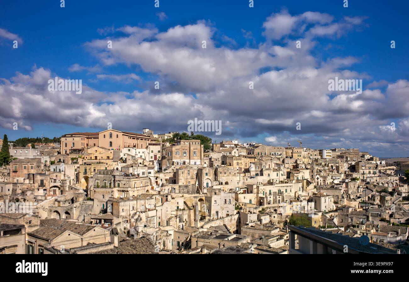 I visitatori camminano per le strade storiche di Matera, vedendo gli antichi edifici in pietra sotto un cielo blu con nuvole. Foto Stock