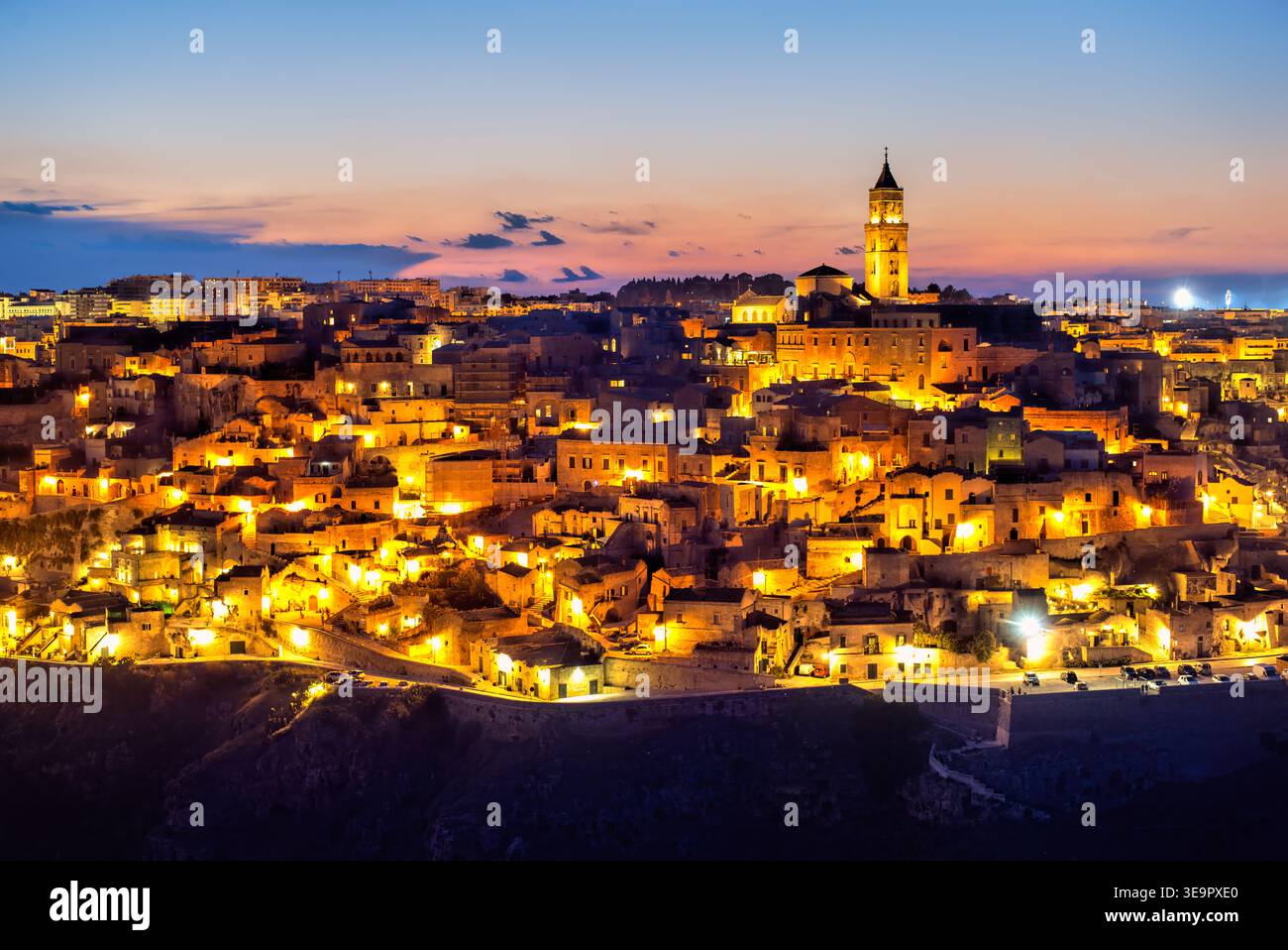 I Sassi di Matera si illuminano al tramonto con luci calde e un cielo limpido. Gli edifici storici si fondono nella notte mentre la città si anima. Foto Stock