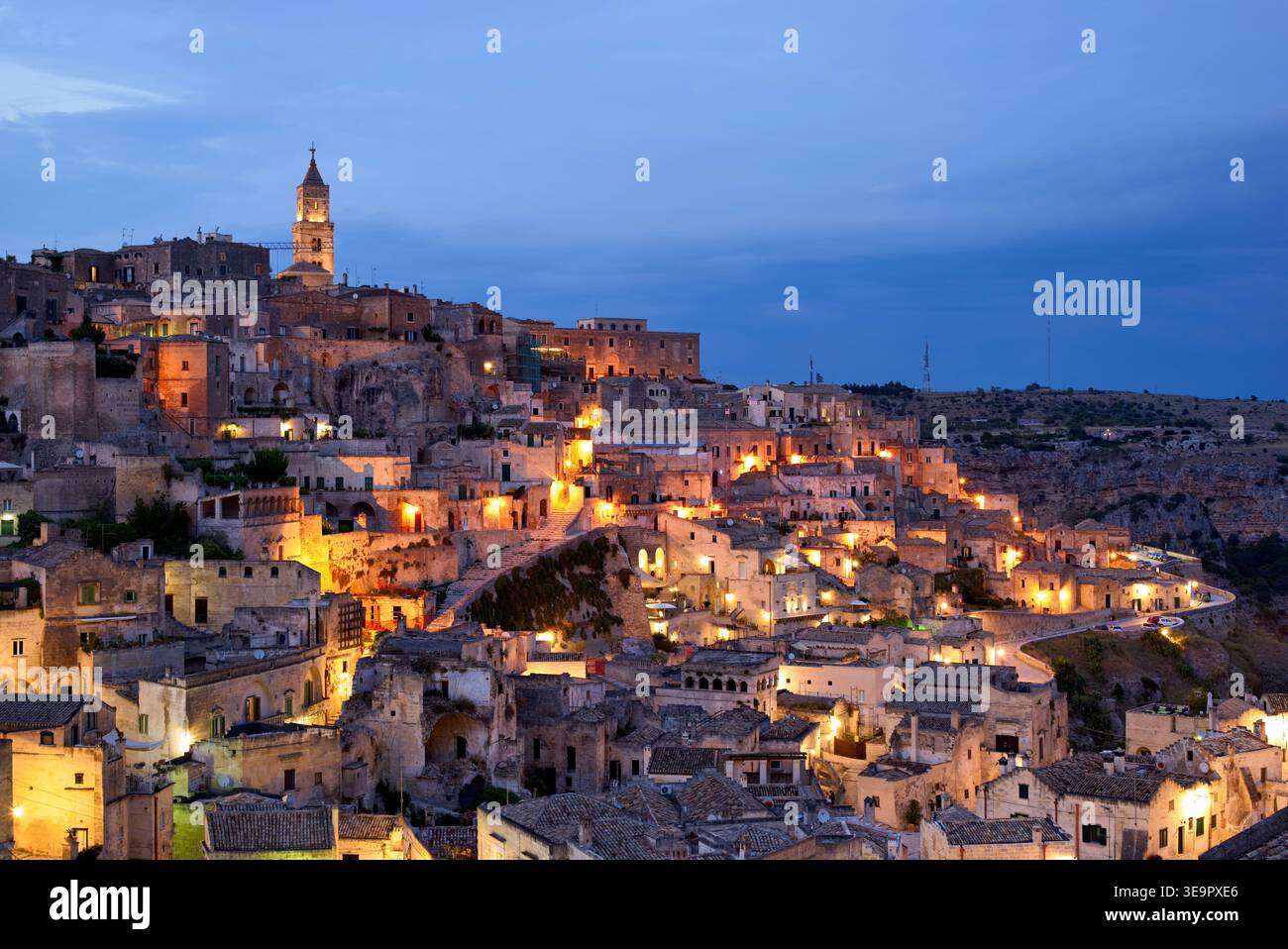 Matera mostra i suoi edifici e le sue strade uniche mentre il sole tramonta. Le luci iniziano a brillare nel cielo serale sopra la città. Foto Stock