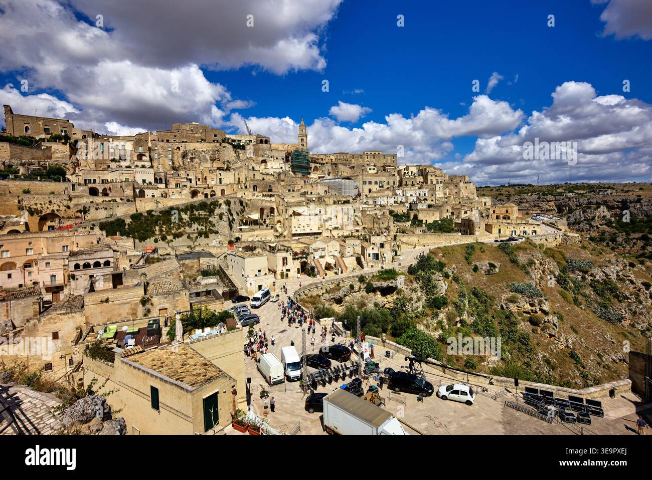I visitatori esplorano le antiche strutture in pietra di Matera in Basilicata, in Italia, sotto un cielo blu brillante con alcune nuvole. Foto Stock