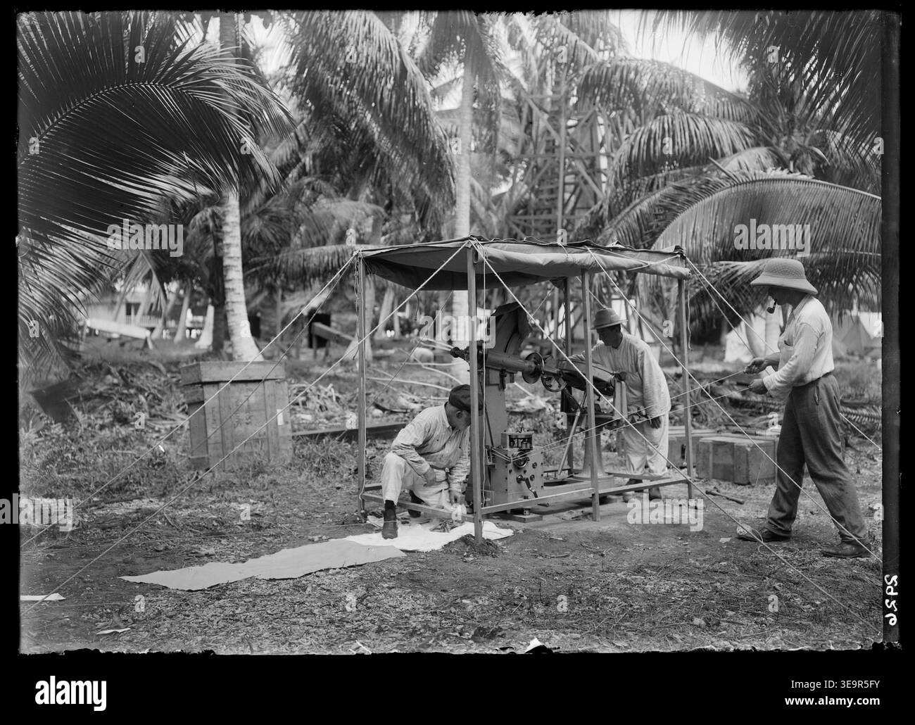 Questa fotografia del 1907 mostra i membri della spedizione di Flint Island che erigono il siderostat di F.K. McClean. La scena raffigura J.W. Short, Joseph Brooks e F.K. McClean che regolano la grande cornice sotto una tela, con il paesaggio tropicale e le palme sullo sfondo. L'immagine d'archivio documenta il lavoro scientifico della spedizione. Foto Stock