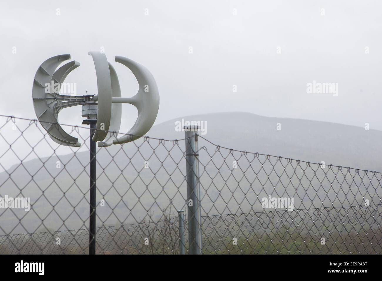 turbina eolica a forma di lanterna posizionata dietro la recinzione. Sfondo montano coperto Foto Stock