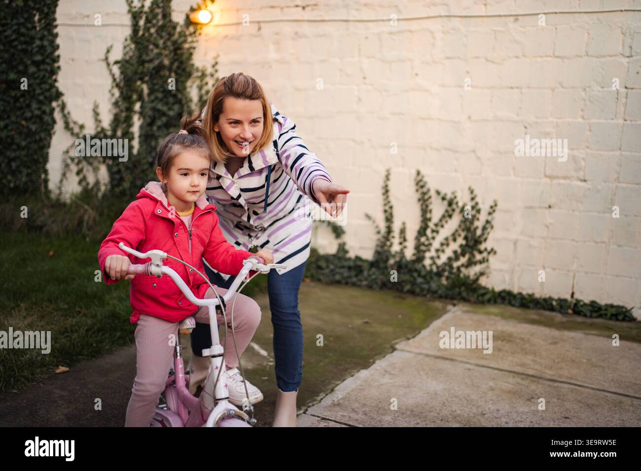 Madre che insegna alla figlia a andare in bicicletta all'aperto, a puntare Foto Stock