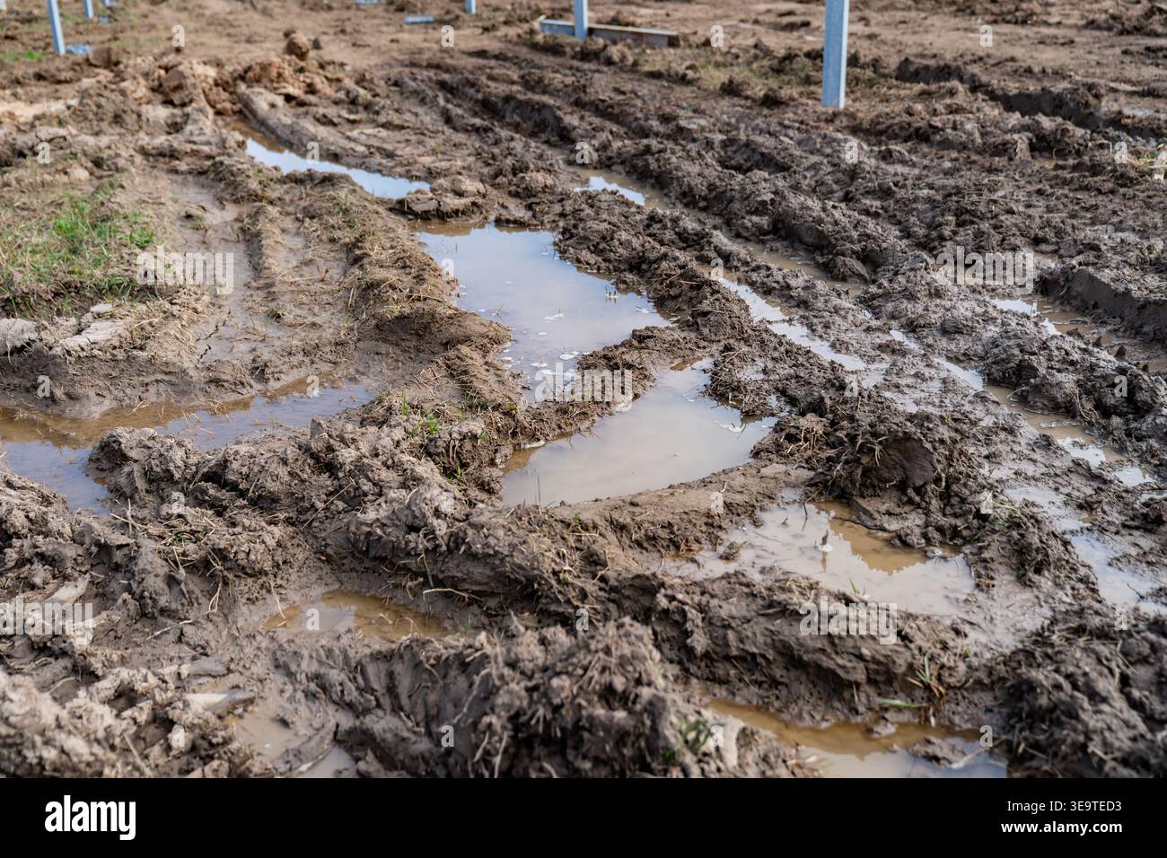 Terreno fangoso del cantiere con pozzanghere d'acqua e cingoli per pneumatici in un progetto di installazione di un impianto a energia solare che rappresenta sfide di sviluppo industriale Foto Stock